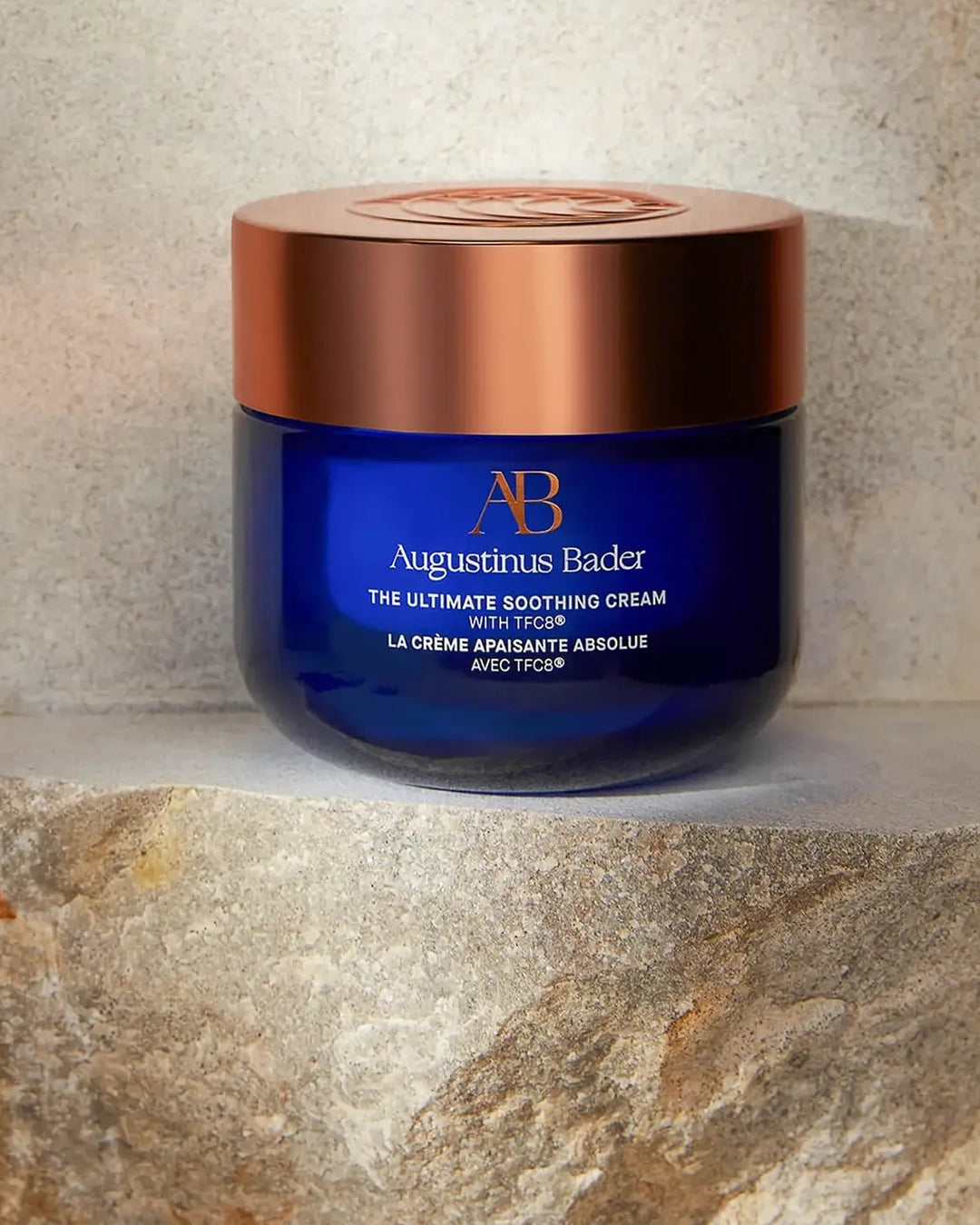 Blue jar of Augustinus Bader cream with a bronze lid on a stone surface