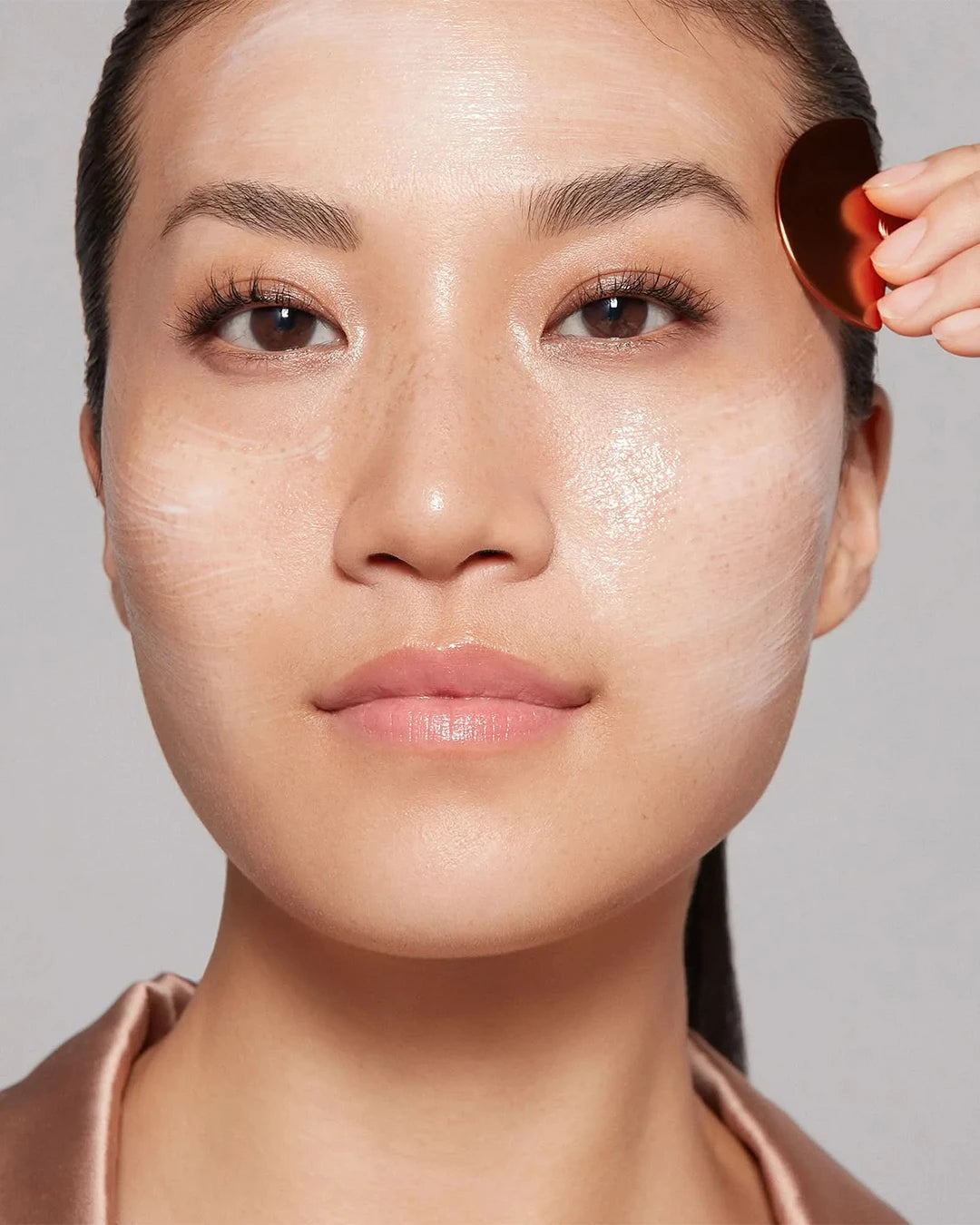 Person applying makeup with a brush on a neutral background