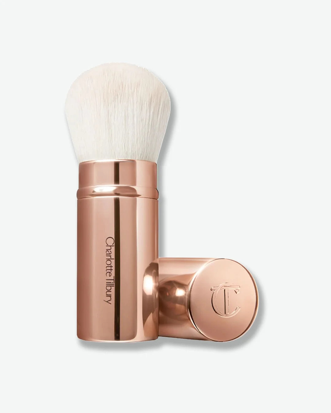 Rose gold makeup brush with rose gold cap off and laid next to the brush with white bristles on a light beige background