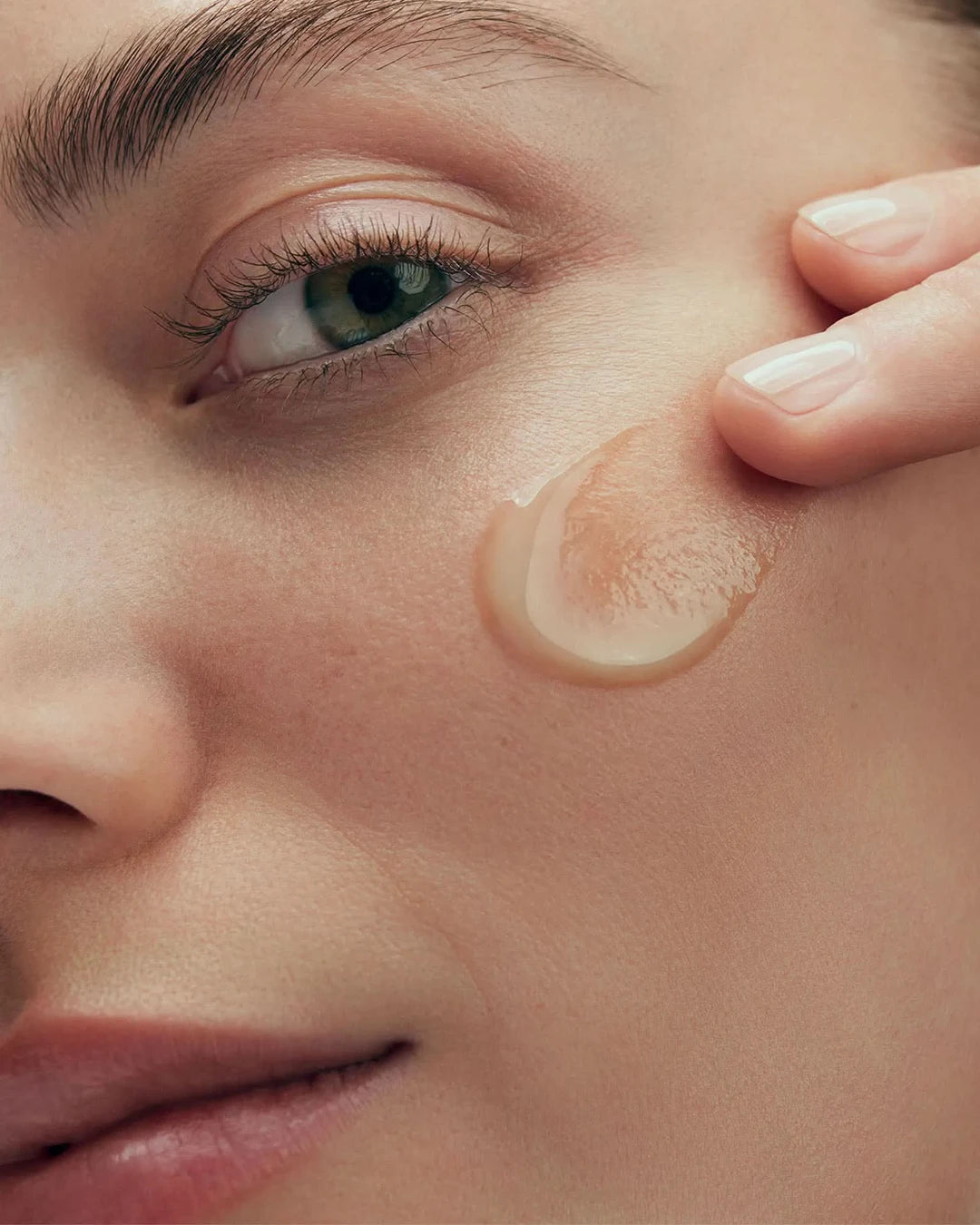 Close-up of a person applying beige cream to their face