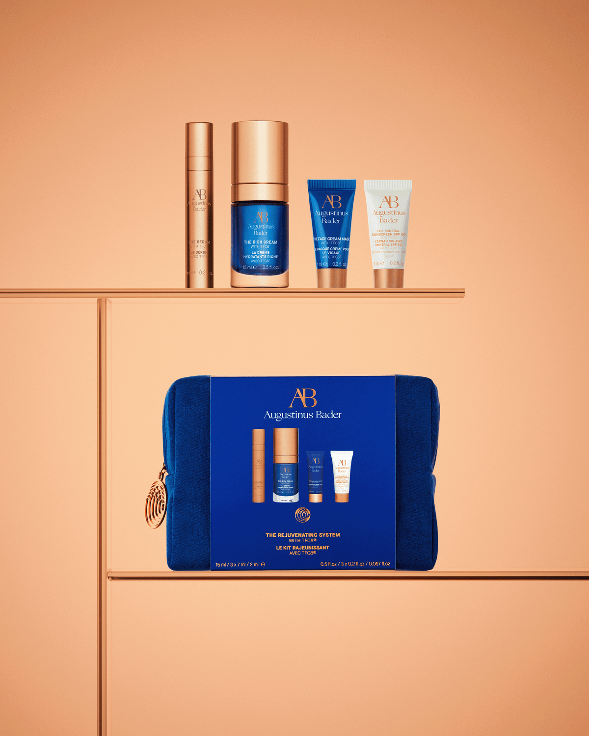 Augustinus Bader The Rejuvenating System products arranged above the blue travel case against a warm peach-toned background.