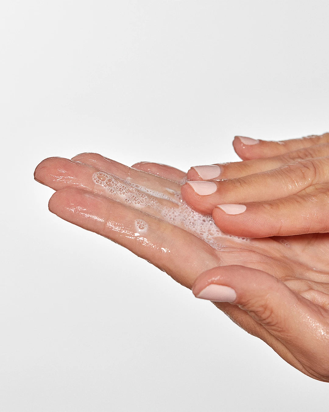 Two hands with soap suds on a light gray background