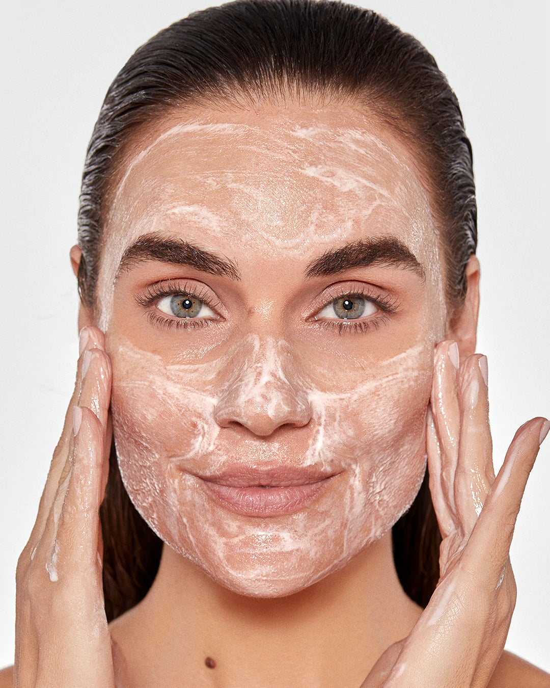 Woman applying a facial mask with a neutral background