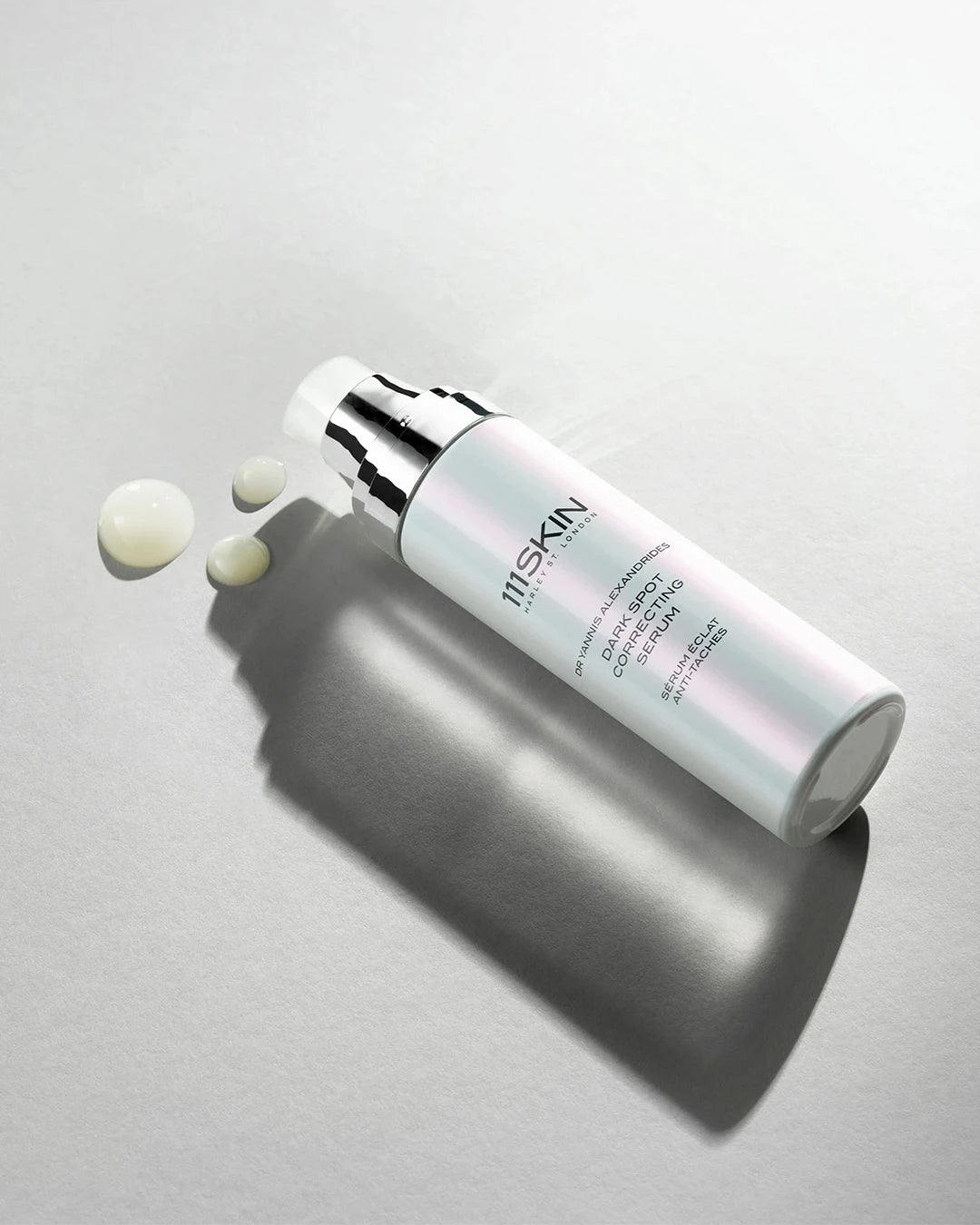 Skincare serum bottle with droplet on a gray background