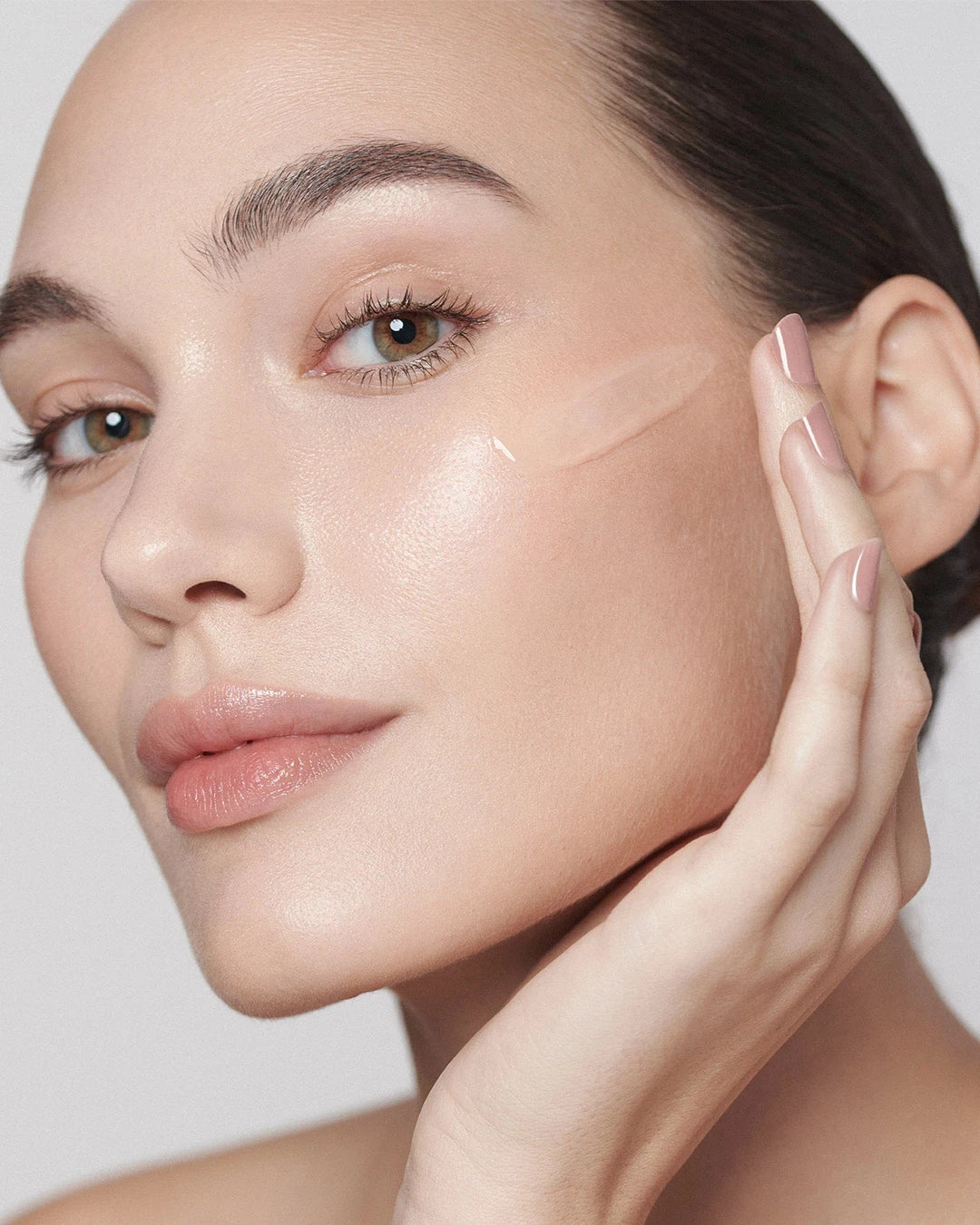 Woman applying a skincare product to her face with a neutral background