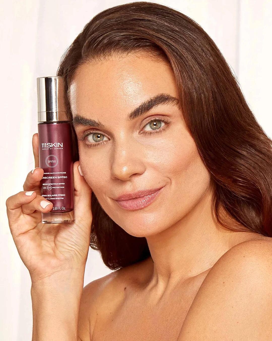 Woman holding a skincare product with a plain background