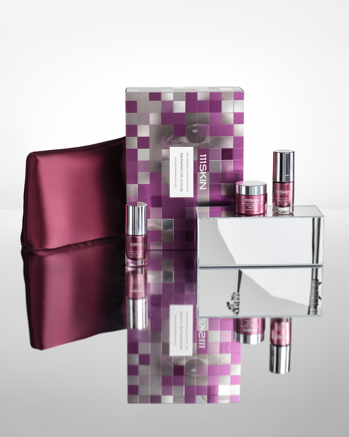 111SKIN Reparative Icons gift set displayed with its purple-and-silver box, burgundy satin pouch, and three skincare treatments.