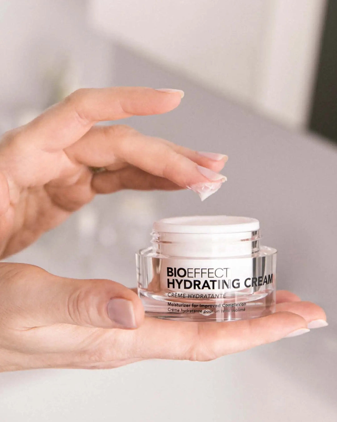 Hand holding a jar of Bioeffect Hydrating Cream against a neutral background