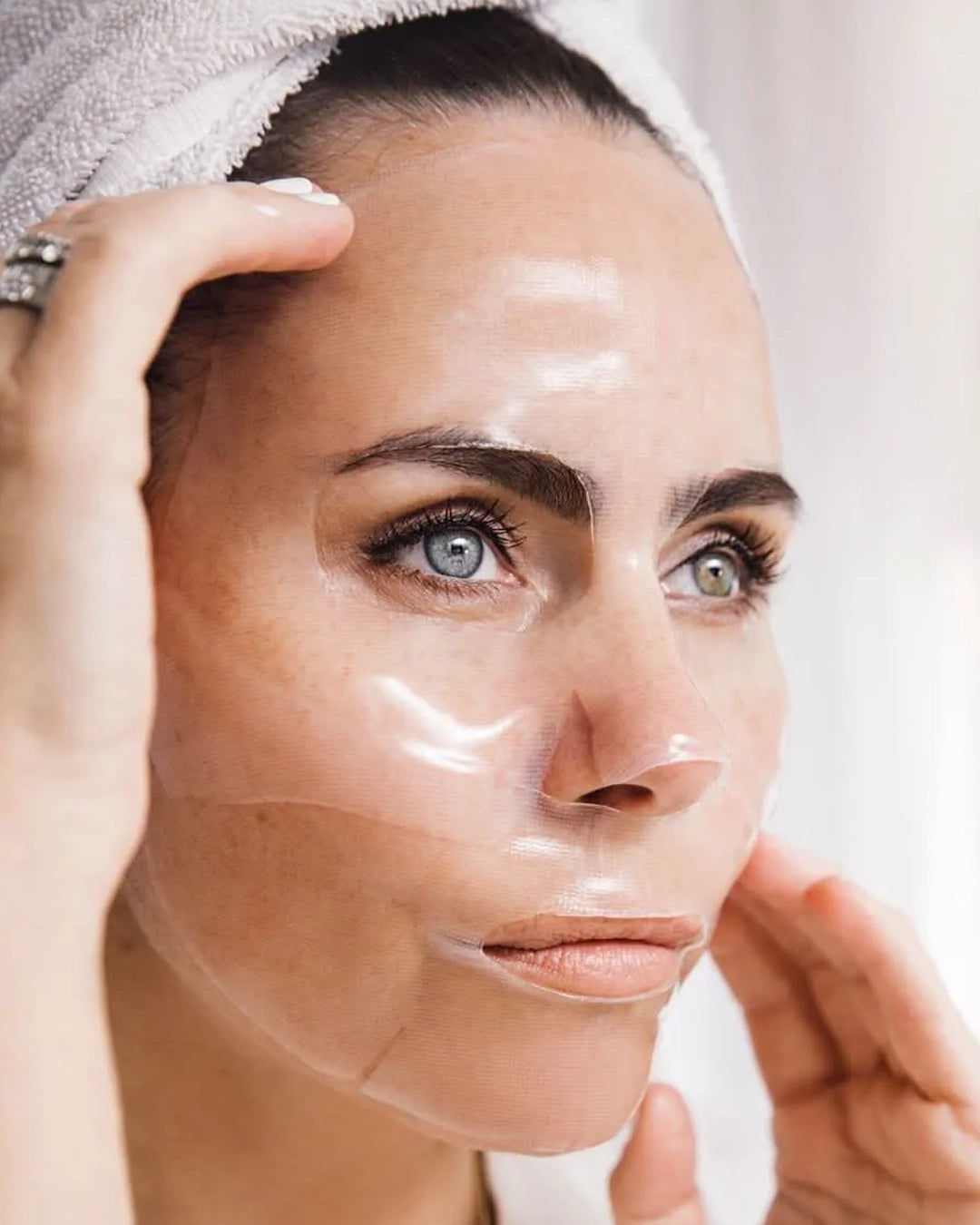 Woman applying a clear facial mask with a towel on her head.