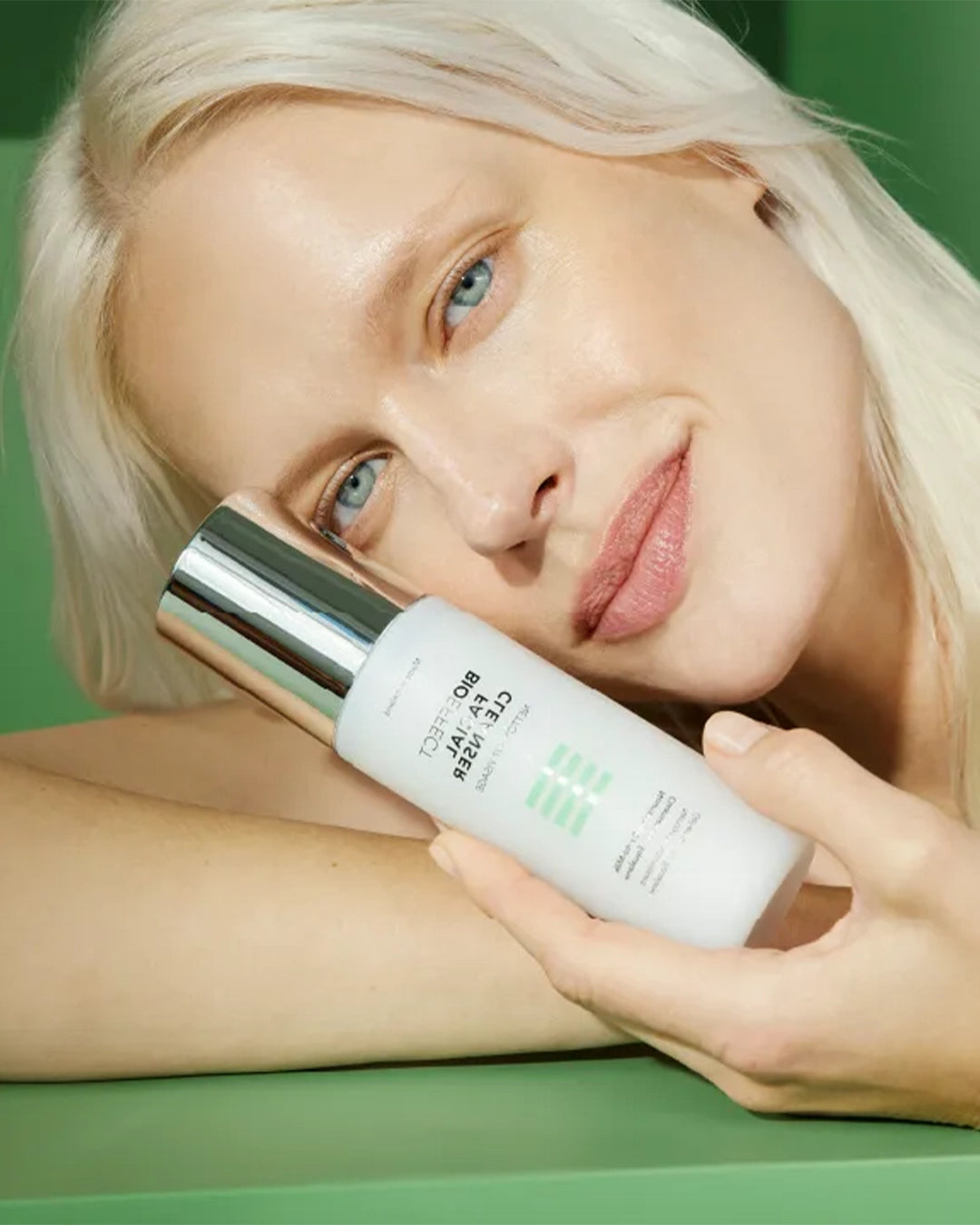 Woman holding a skincare bottle with a green background