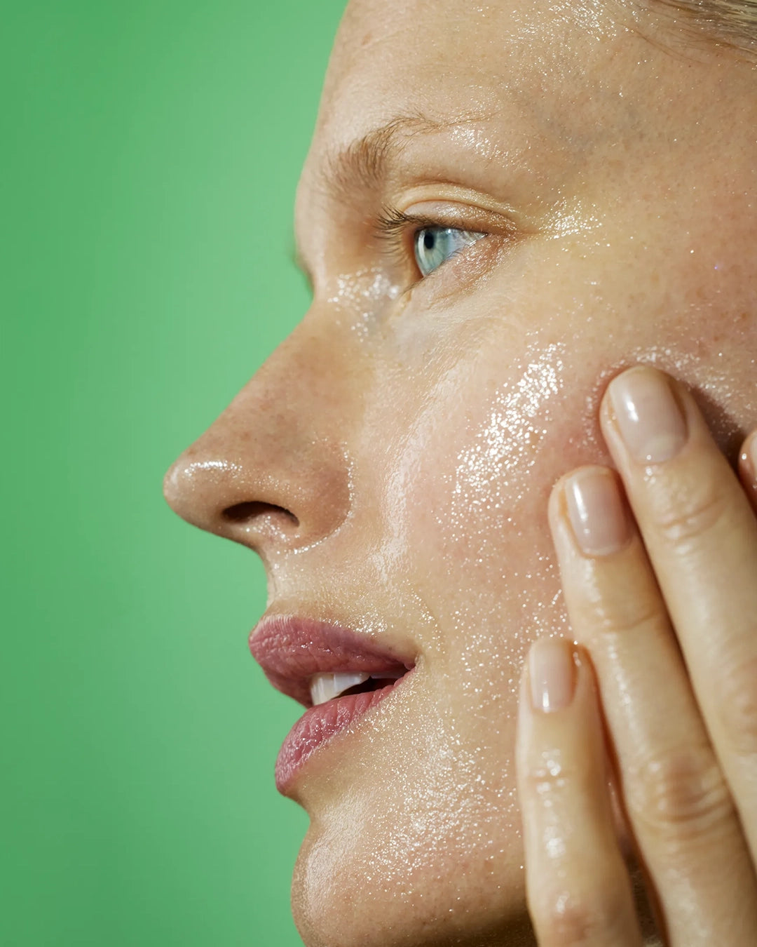 Close-up of a woman applying a skincare product on her face with a green background