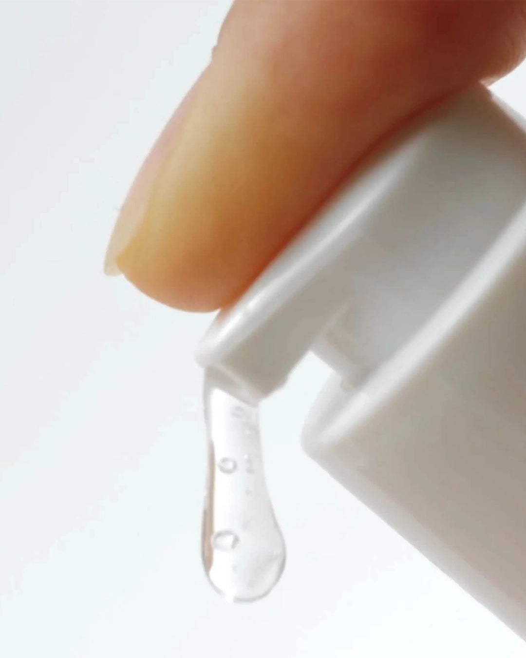 Close-up of a hand holding a white bottle with a dropper, releasing a clear liquid.