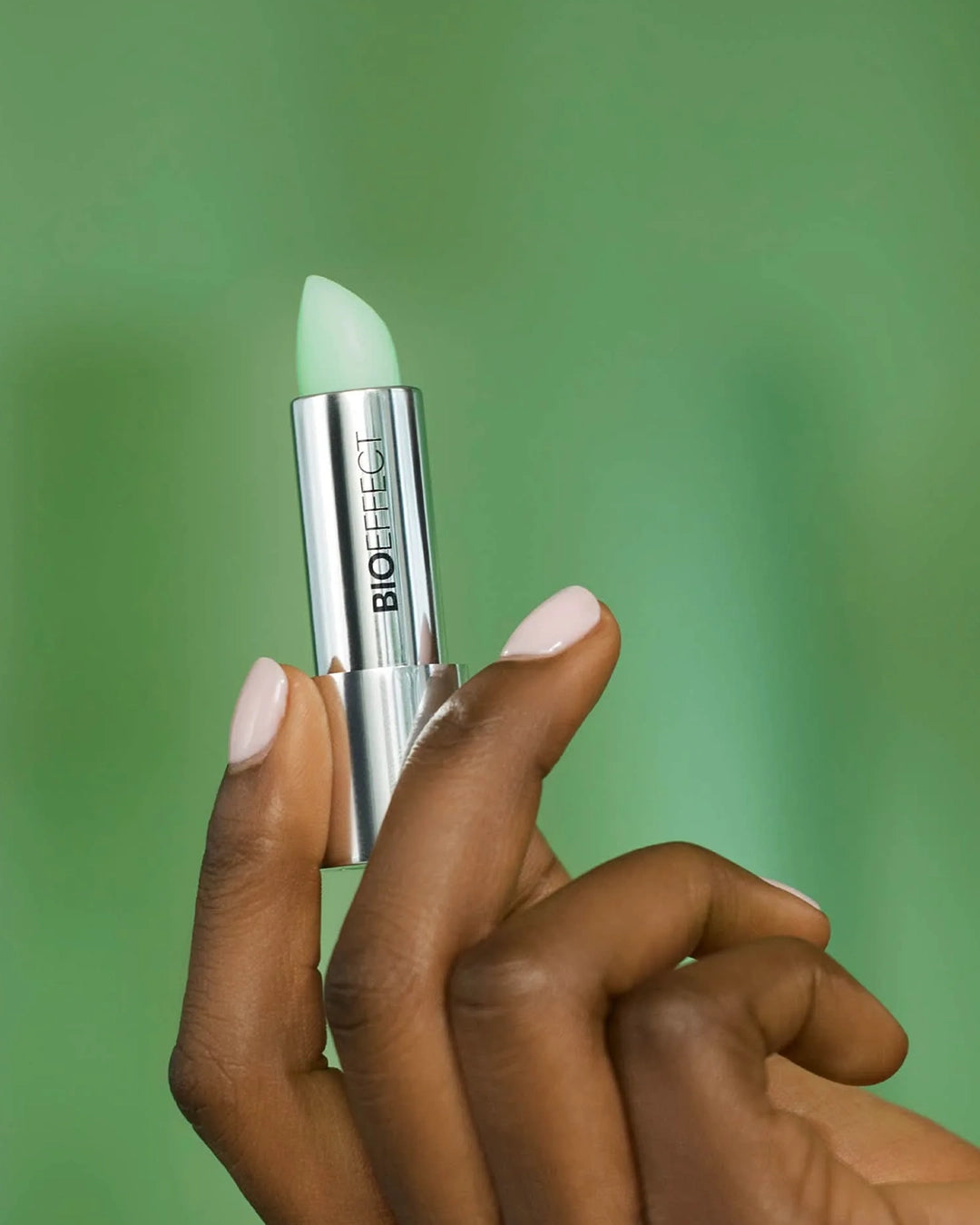 Hand holding a Biorefect lip balm against a green background