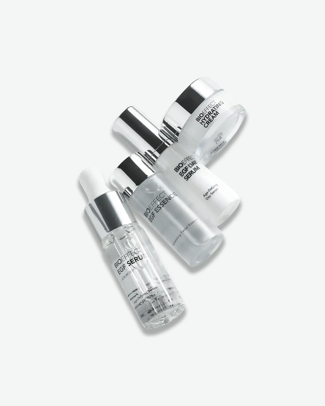 A close-up, top-down shot of four Bioeffect skincare products arranged diagonally. The products include a clear glass dropper bottle of Bioeffect EGF Serum, a frosted glass bottle of Bioeffect EGF Essence, a white bottle of Bioeffect EGF Day Serum, and a small glass jar of Bioeffect Hydrating Cream, all featuring metallic silver caps.