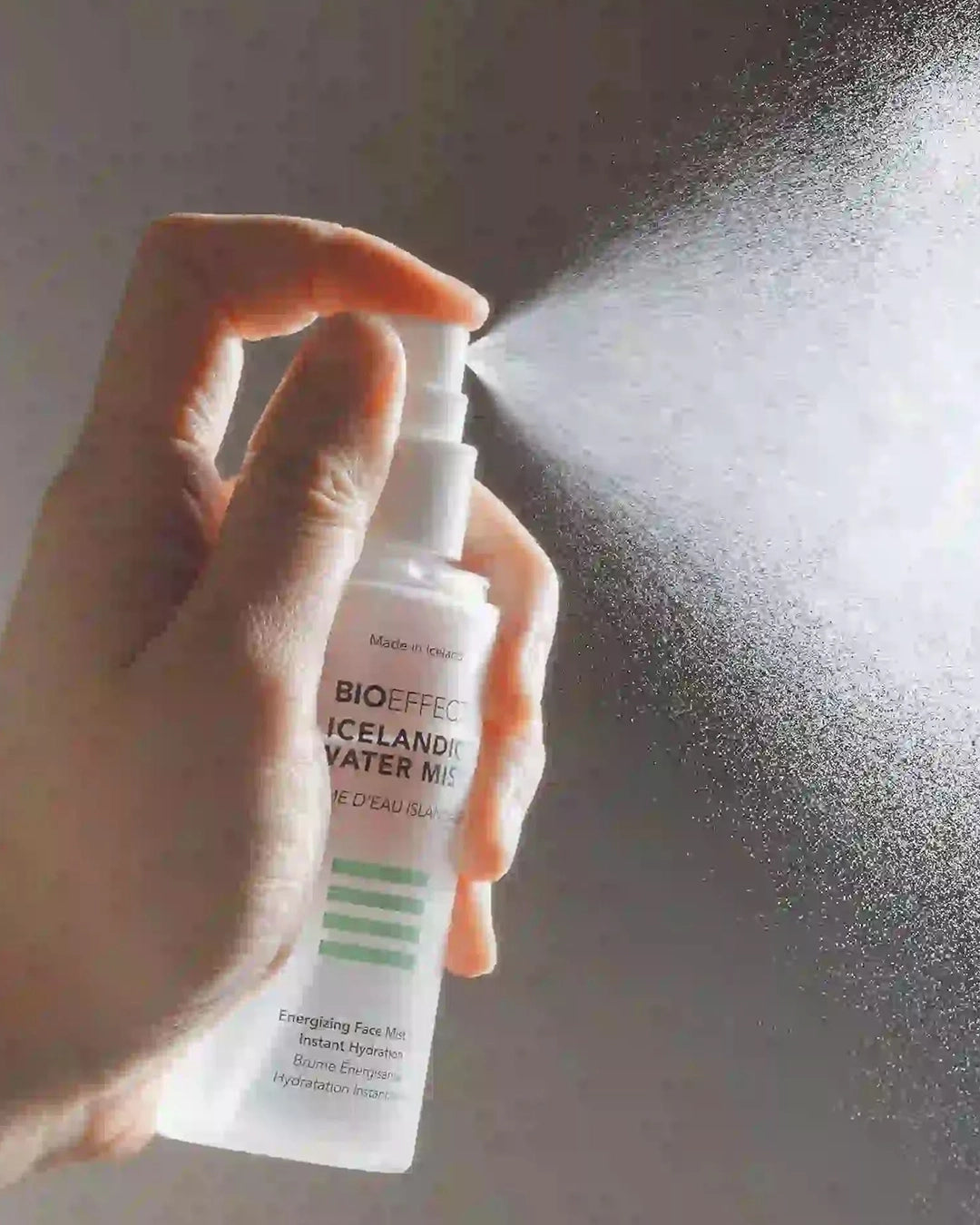 Hand holding a Bioeffect spray bottle and spraying it against a neutral background