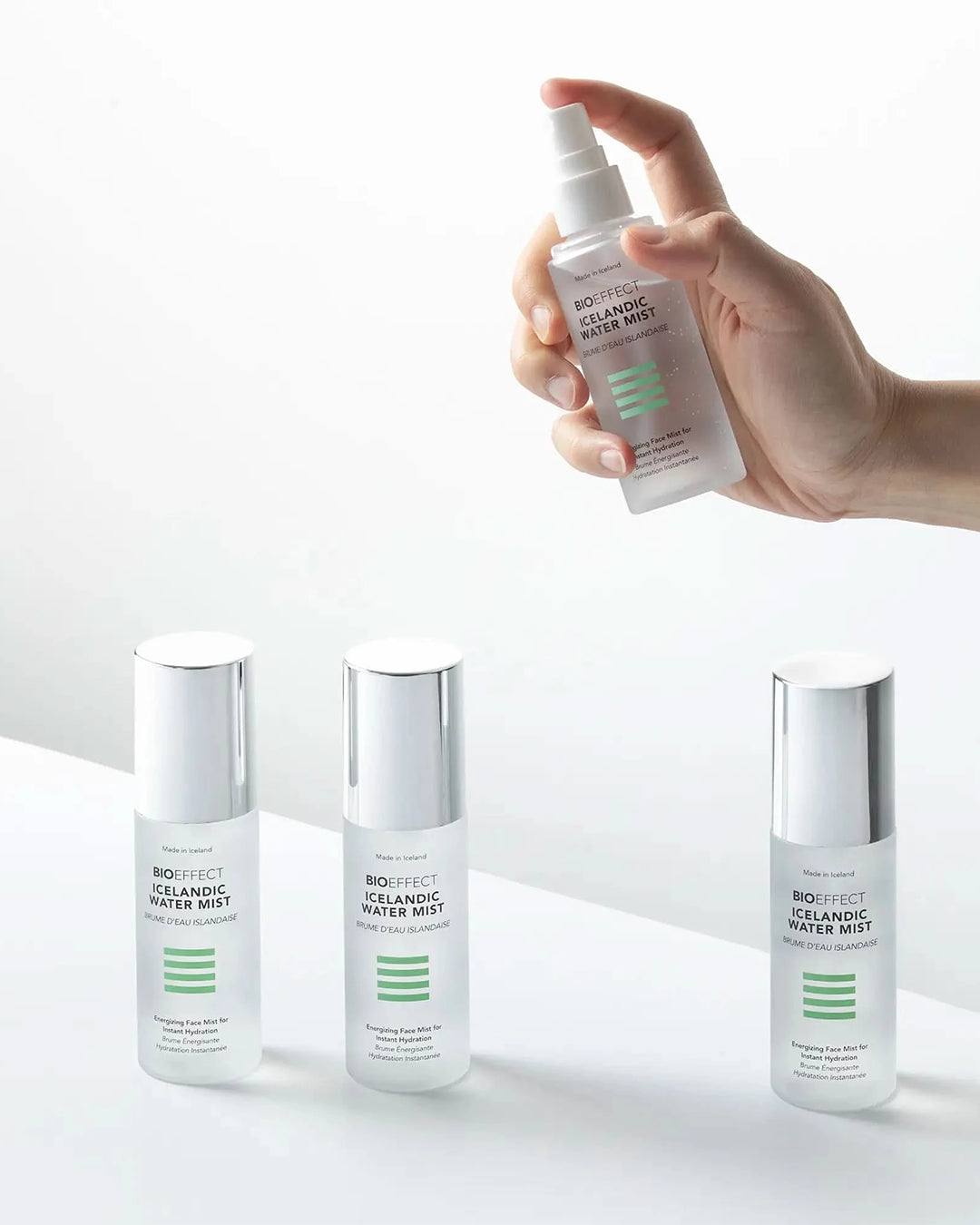 Hand holding a spray bottle of skincare product with other bottles on a light background