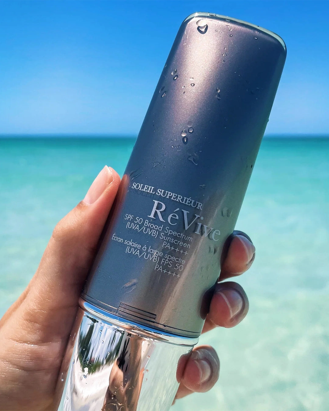 Revive sunscreen bottle held in front of a beach