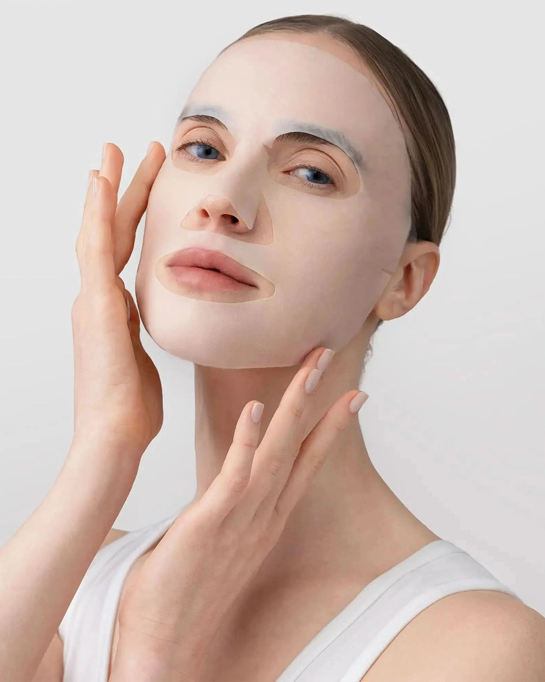 Woman applying a white facial mask on a light background