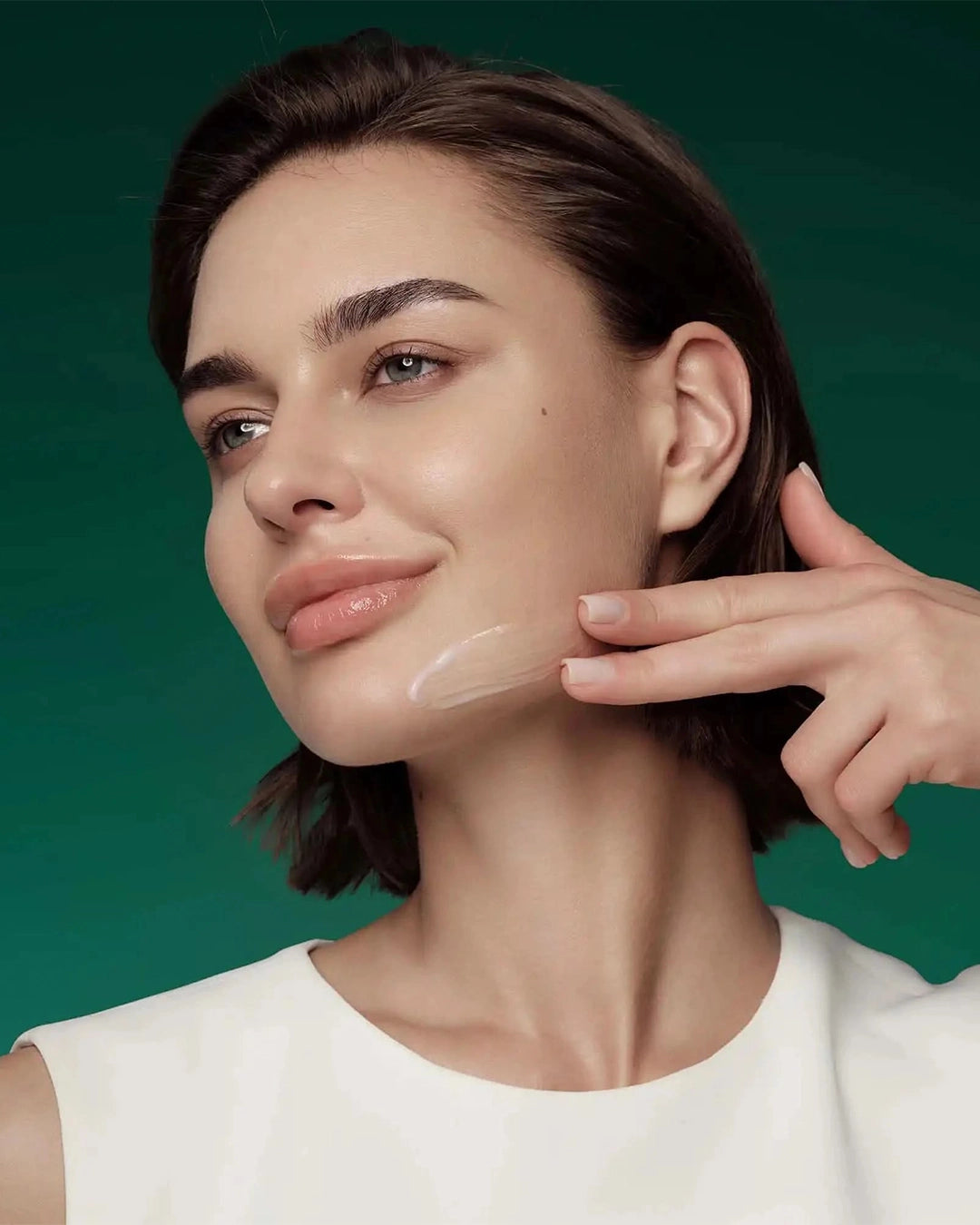 Woman applying cream to her face with a green background