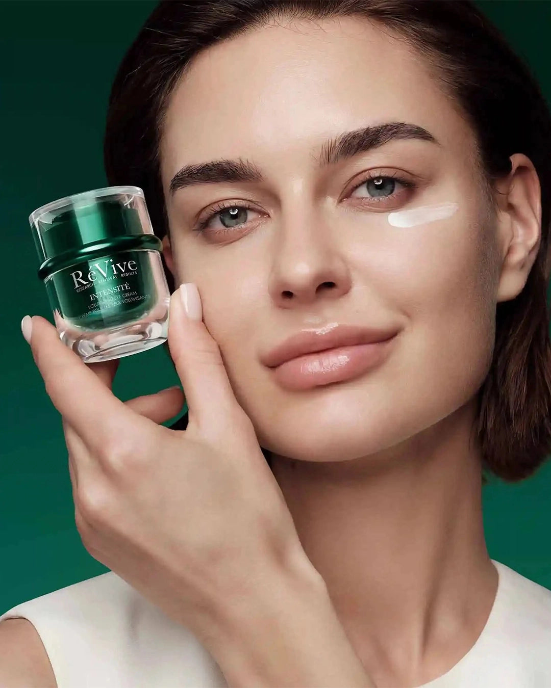Woman holding a jar of Re Vive skincare product against a green background