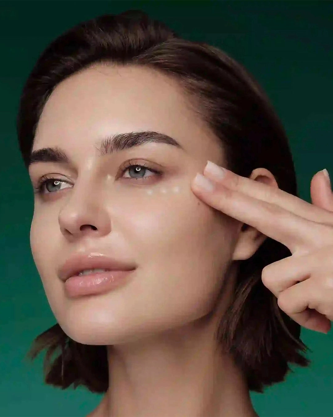 Woman pointing to product on her face against a green background