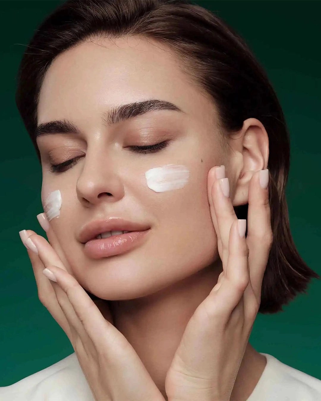 Woman applying cream to her face with a green background