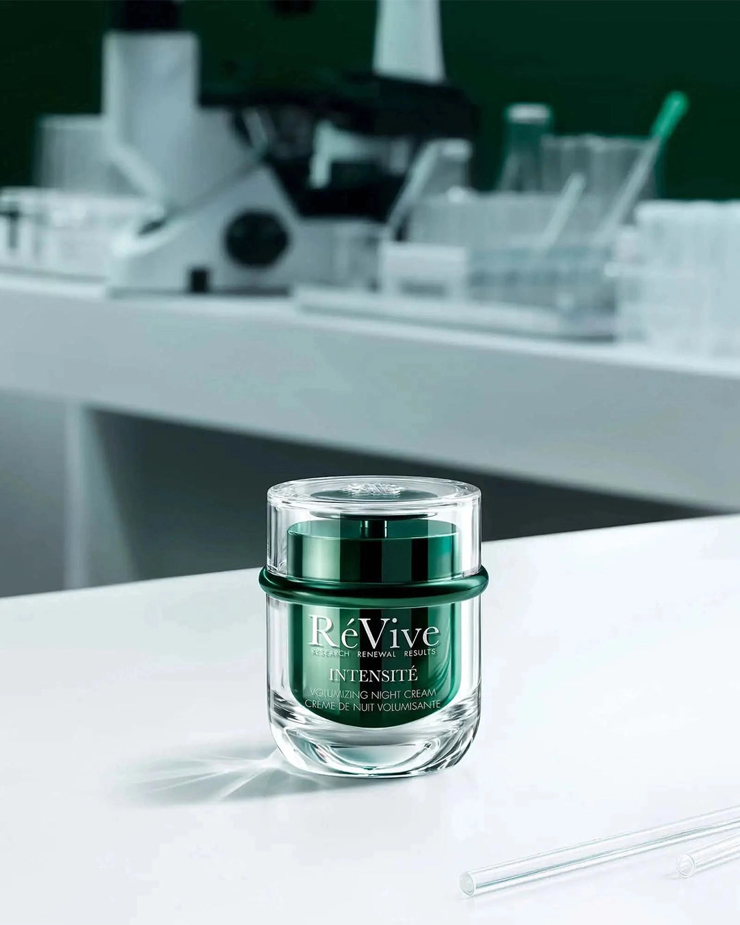 Green skincare jar labeled 'Re Vive' on a white surface with blurred laboratory equipment in the background.