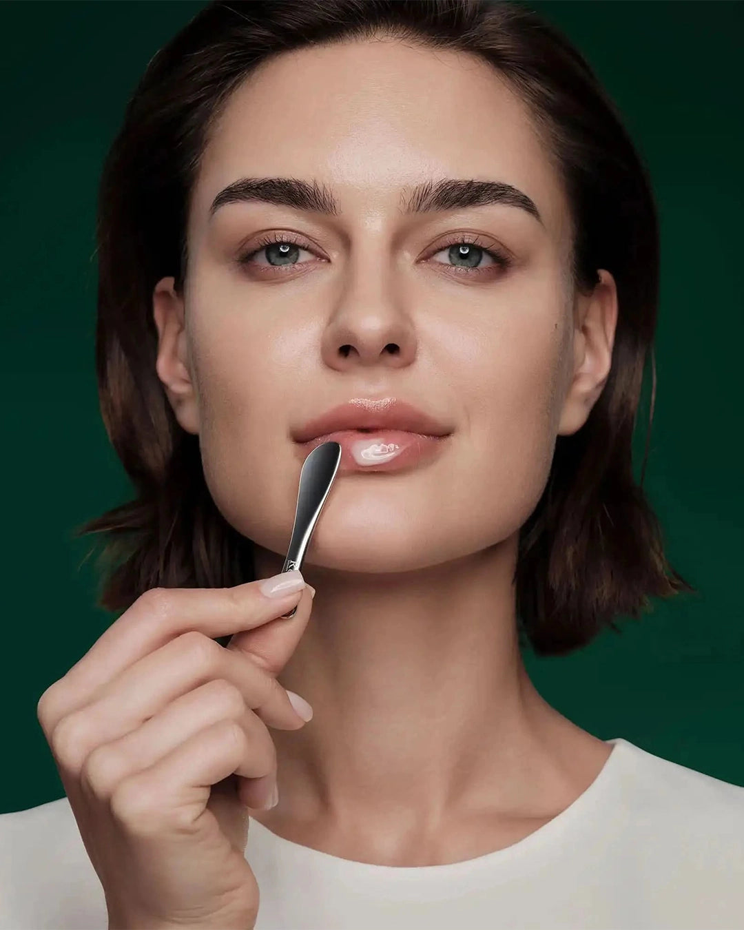 Woman holding a small applicator tool to her face against a green background