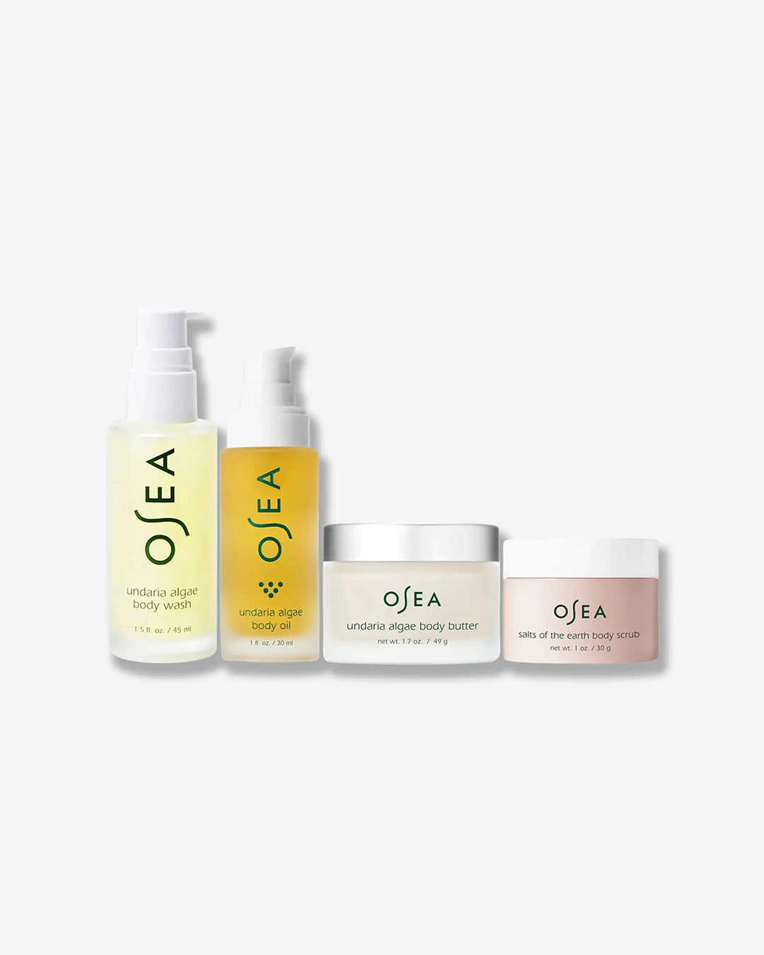 A product group shot showcasing four OSEA travel-sized items arranged by height on a white surface: a translucent yellow body wash, a golden body oil bottle, a clear jar of body butter, and a frosted pink jar of salts of the earth body scrub.