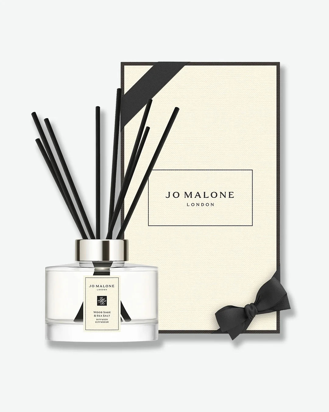 Jo Malone London Wood Sage & Sea Salt reed diffuser standing in front of its black and cream presentation gift box with a matching cream bow.
