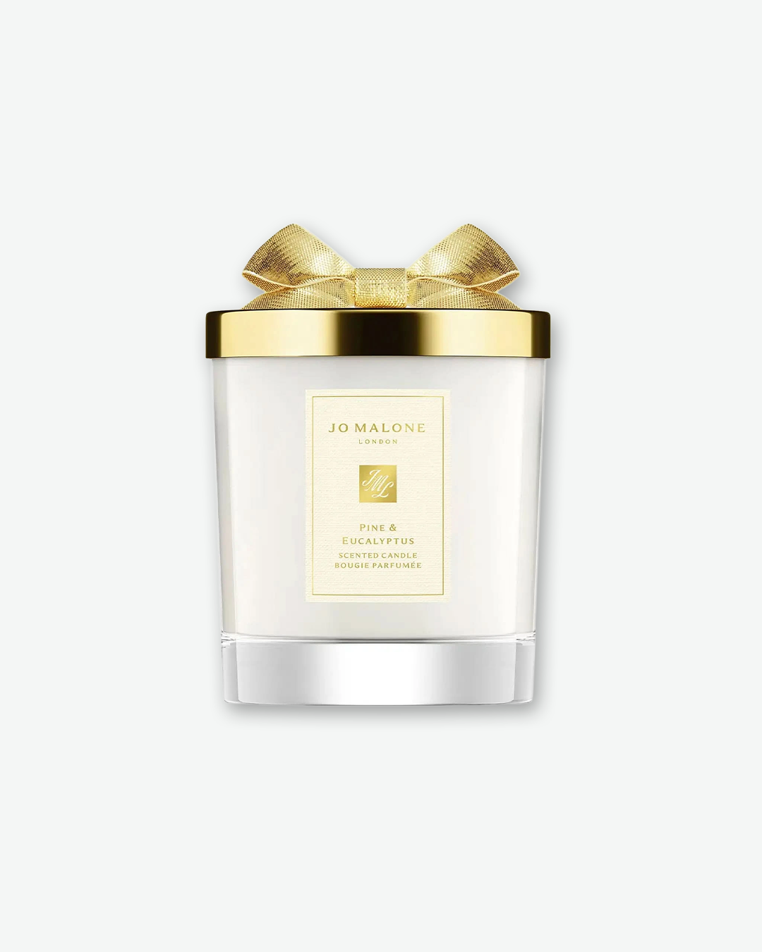 Product image of a Jo Malone London Pine & Eucalyptus scented candle. The white wax is housed in a clear, frosted glass container featuring a textured cream label with gold writing. The candle is topped with a polished, metallic gold lid decorated with a sculpted gold bow, shown against a solid pale gray background.