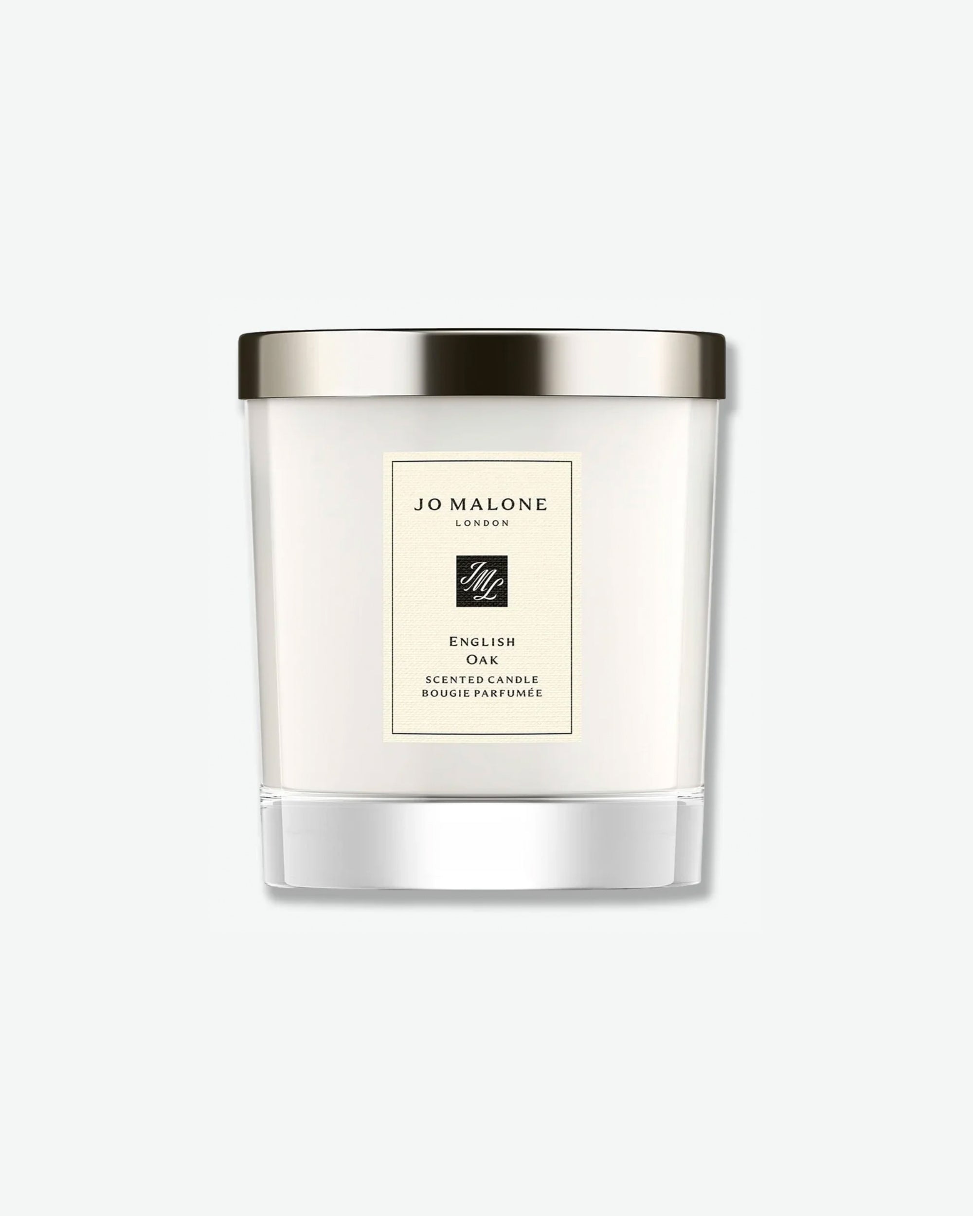 Front view of a Jo Malone London English Oak scented candle. The candle features cream-colored wax inside a clear glass jar with a thick, transparent base and is topped with a polished, metallic silver lid. A rectangular cream label on the front features a black border, the Jo Malone logo, and text that reads "English Oak Scented Candle / Bougie Parfumée."