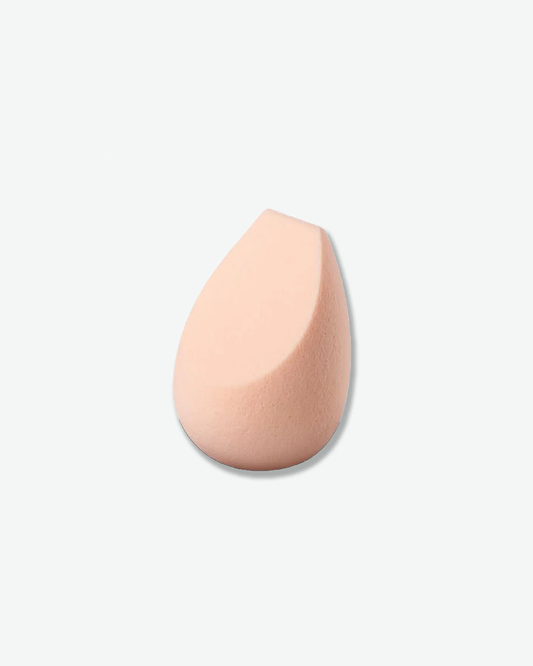 A light peach-colored teardrop-shaped makeup blending sponge with a flat angled edge on one side, shown against a light grey background.