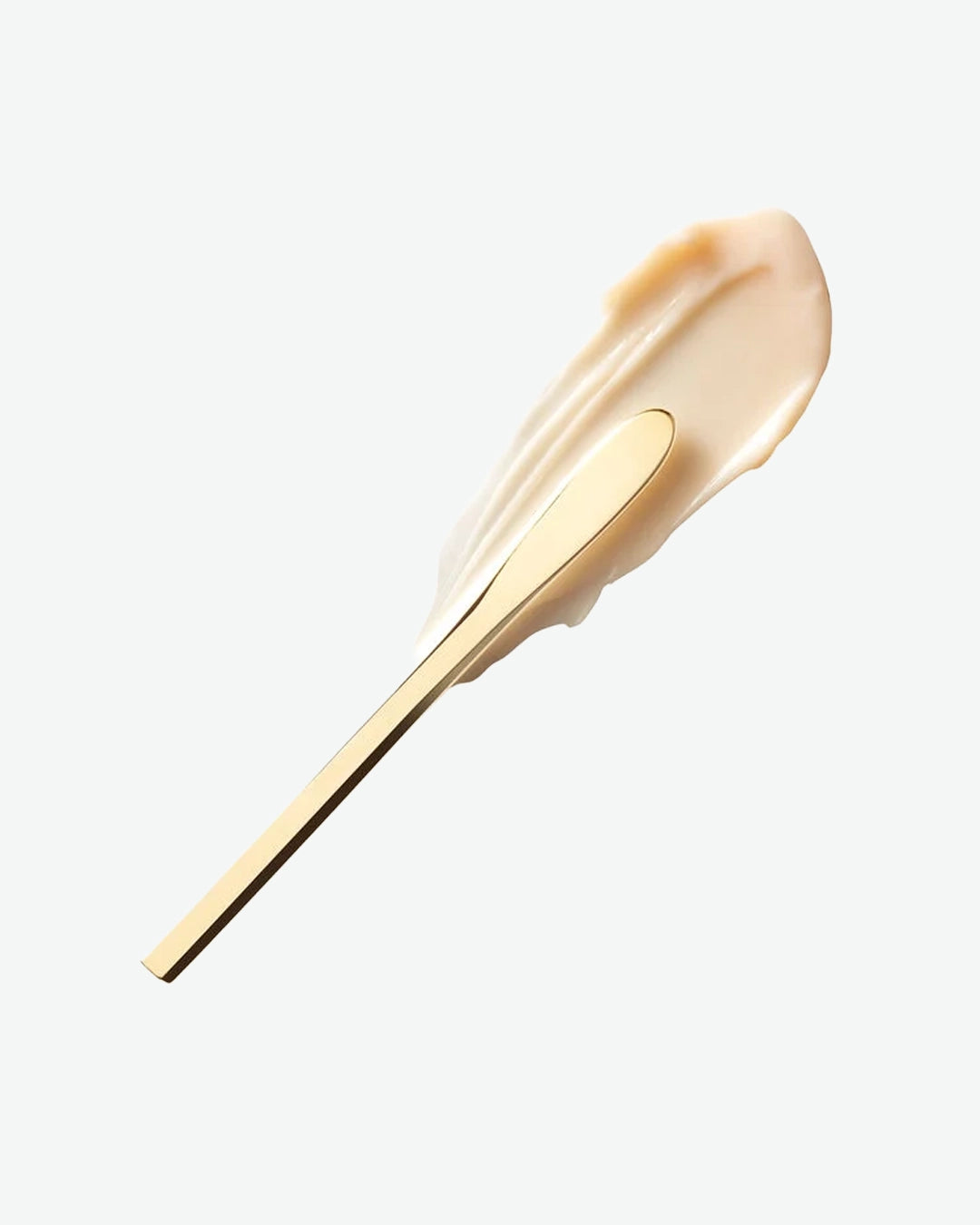 Close-up of a cream texture swatch with gold applicator tool on a white background