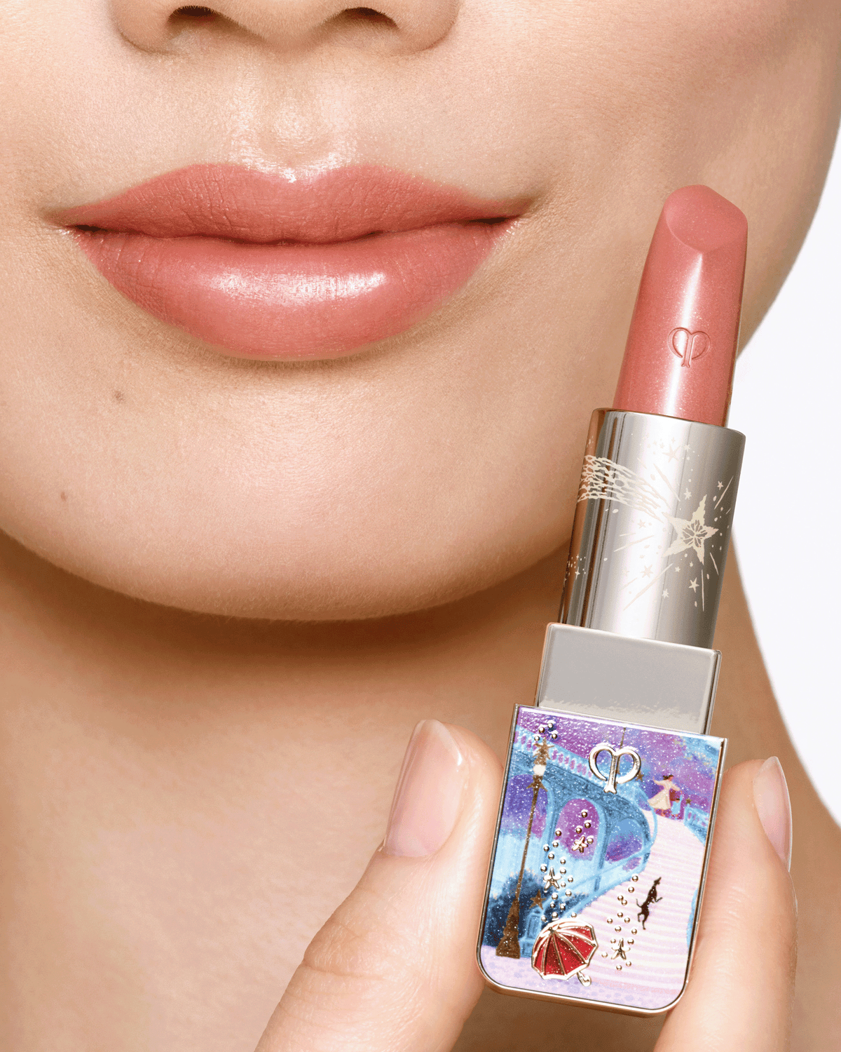 Close-up of a model wearing glossy rosy nude lipstick while holding the Clé de Peau Beauté limited-edition holiday lipstick.