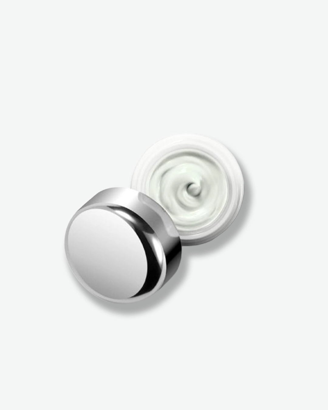 An overhead product shot of an open La Mer skincare jar, centered against a plain light gray background. The small white glass jar is open, revealing a smooth, thick white eye cream swirled inside. Resting partially over the side of the opening is its highly reflective chrome silver dome cap.