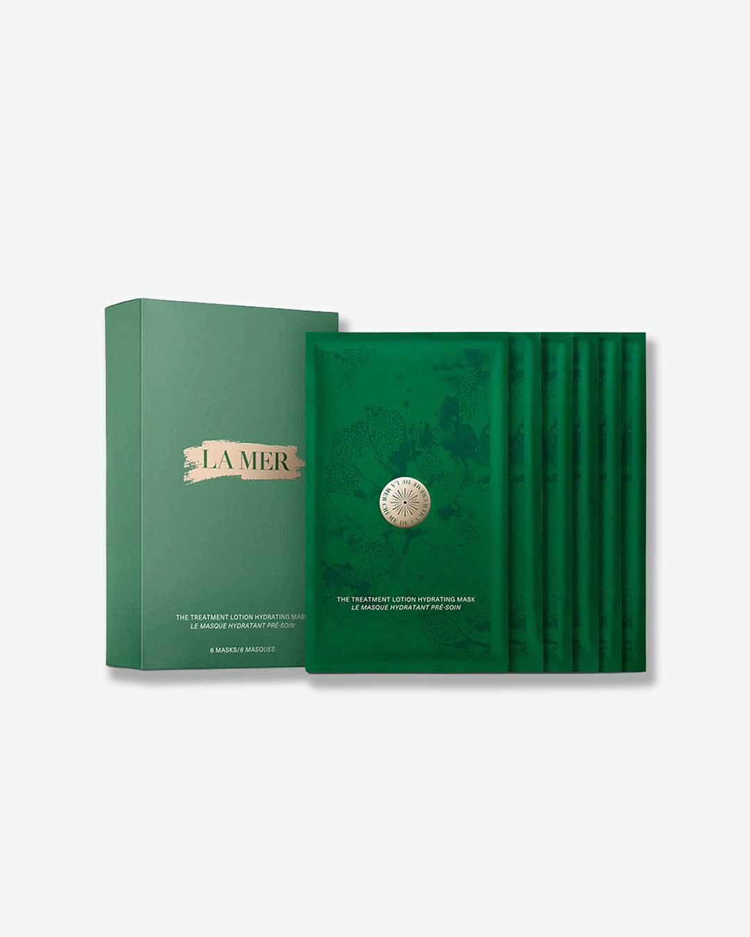 A La Mer skincare set featuring a sage green vertical product box alongside a fanned-out row of six deep emerald green sheet mask sachets. The box displays the "LA MER" brand name over a metallic gold brushstroke background, with the product name "THE TREATMENT LOTION HYDRATING MASK / LE MASQUE HYDRATANT PRÉ-SOIN" and "6 MASKS / 6 MASQUES" printed in white near the bottom. The front mask sachet features a subtle, tonal botanical pattern, a circular gold emblem in the center, and matching product text at the