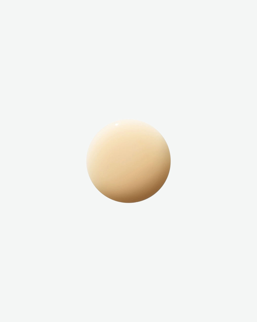 A close-up swatch of La Mer The Lifting Firming Serum is displayed against a light gray background. The pale golden-beige formula appears as a smooth, glossy droplet, highlighting its lightweight texture and luxurious consistency. The image showcases the serum’s silky appearance and refined finish.