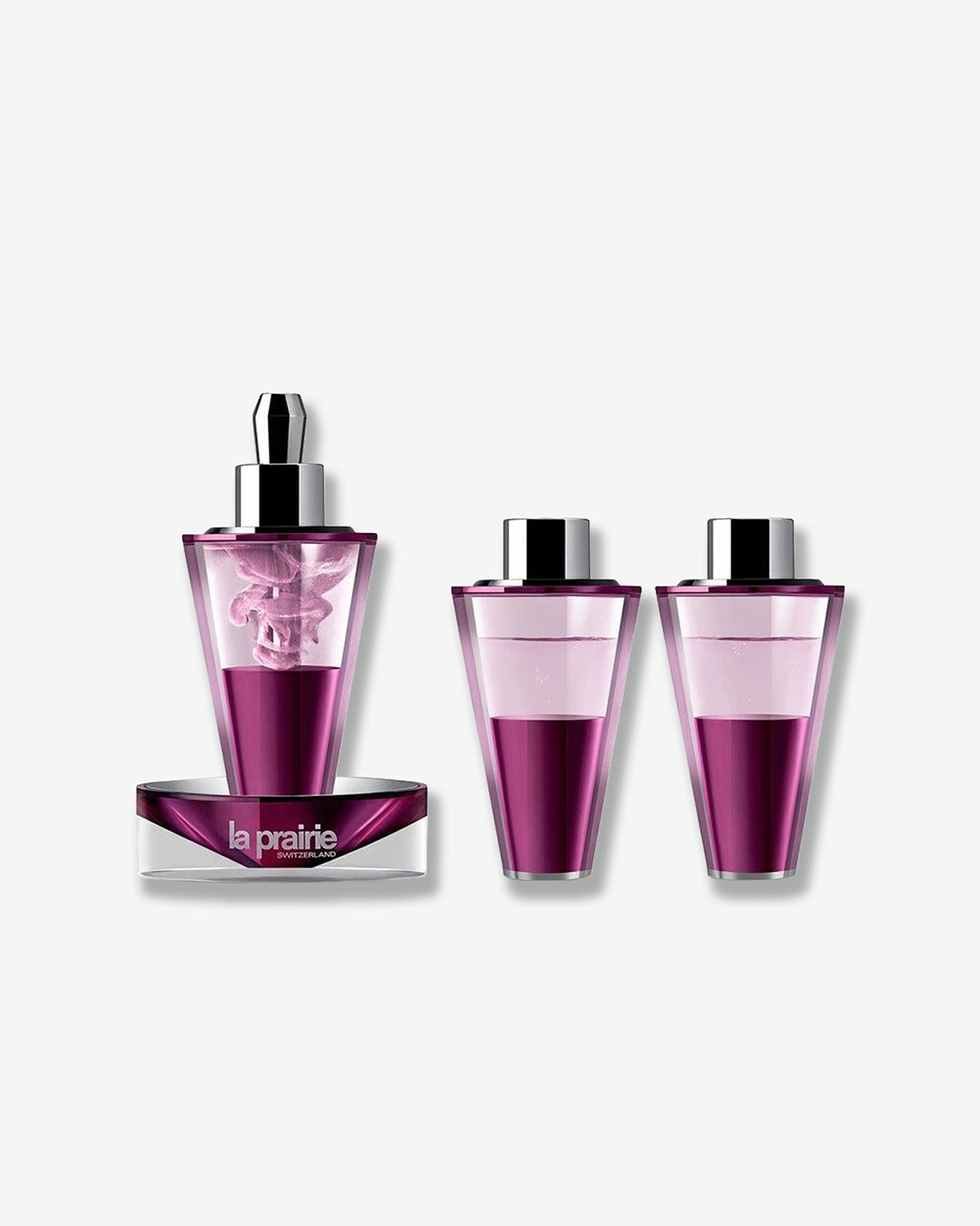 A product shot of the La Prairie Platinum Rare skincare set outside its packaging. It features three futuristic, cone-shaped purple and silver vials, with the main dropper vial resting on a clear, branded base showing swirling pink-purple liquid inside.