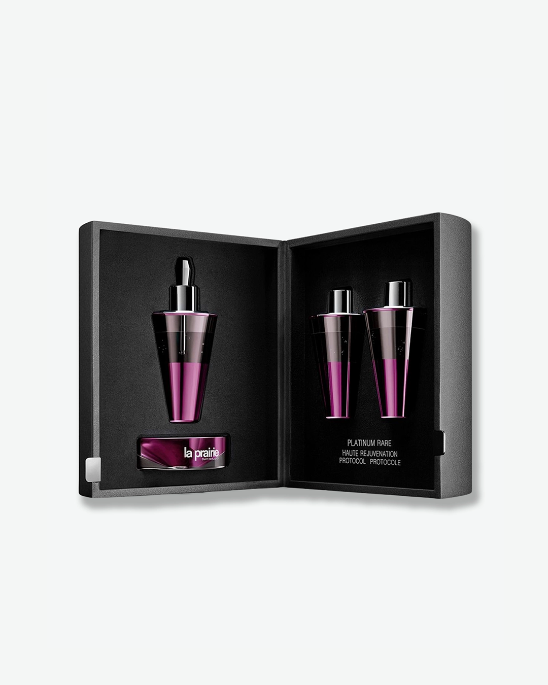 An elegant, open textured black presentation case showcasing the La Prairie "Platinum Rare Haute Rejuvenation Protocol." Inside the custom-molded black interior are three metallic purple and silver vials, with one resting on a small matching base labeled "la prairie SWITZERLAND".