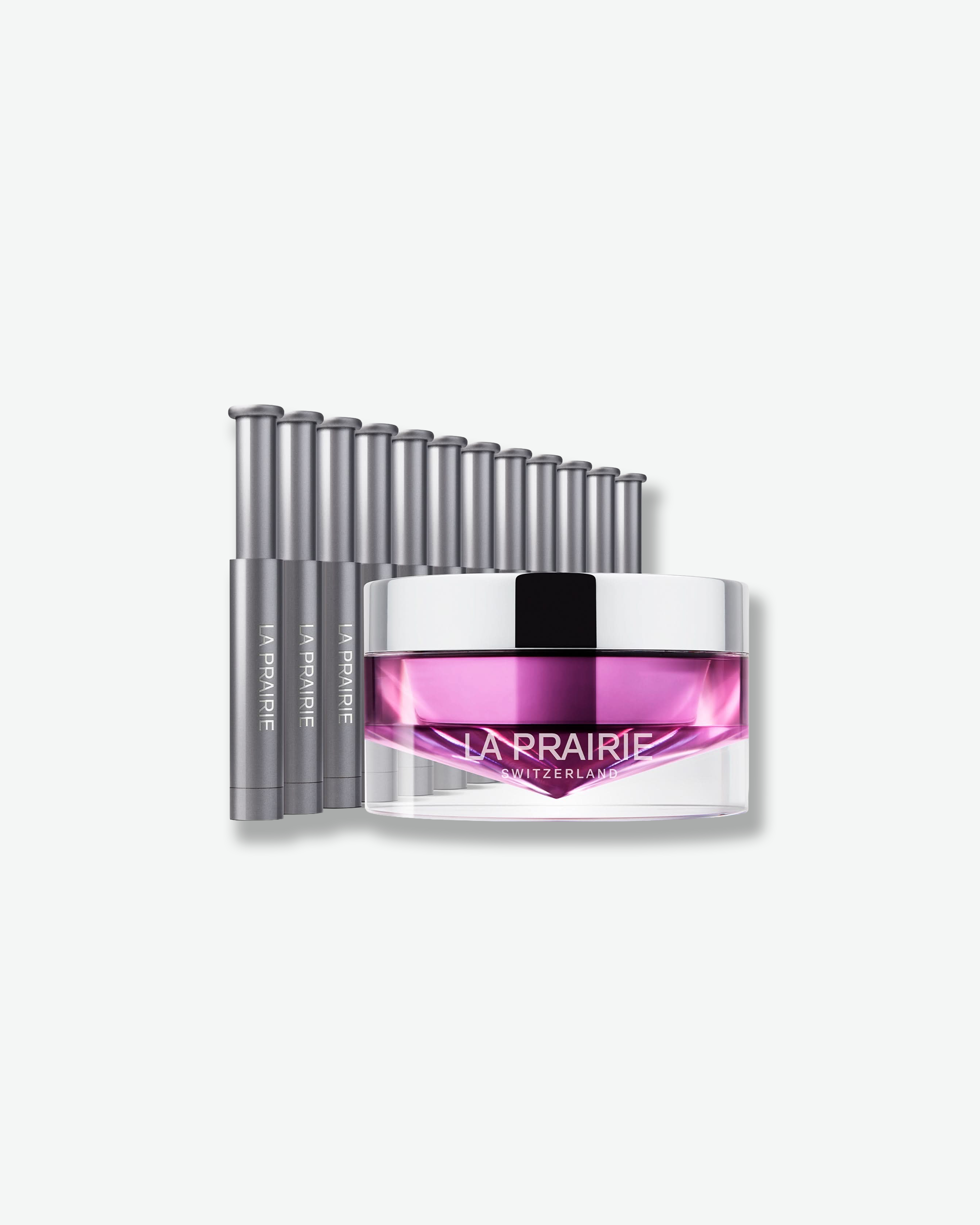 La Prairie Platinum Rare Haute-Rejuvenation Mask set, featuring a round, clear glass jar with a faceted violet-purple interior and a silver lid, positioned in front of twelve slender metallic silver serum vials lined up on a plain light gray background.