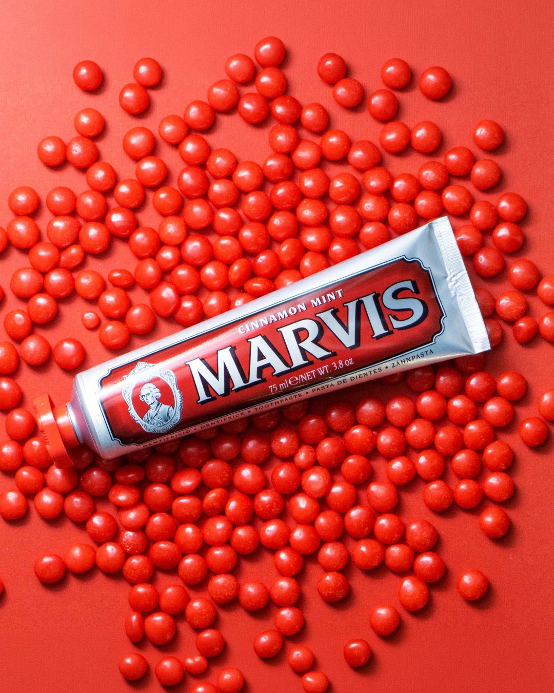 Marvis toothpaste tube surrounded by red candies on a red background