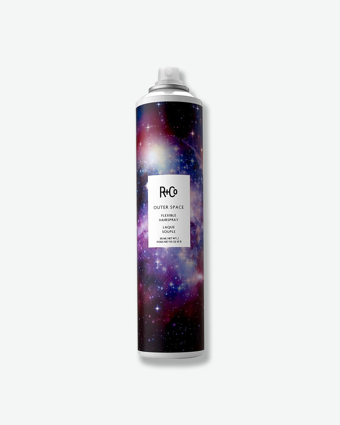 Product image of R+Co Outer Space Flexible Hairspray displayed against a light gray background. The aerosol can features the brand’s signature galaxy-inspired artwork in vibrant shades of purple, blue, and pink, with a white spray nozzle and minimalist label. The image highlights the flexible-hold hairspray designed to provide long-lasting style while maintaining movement and touchability.