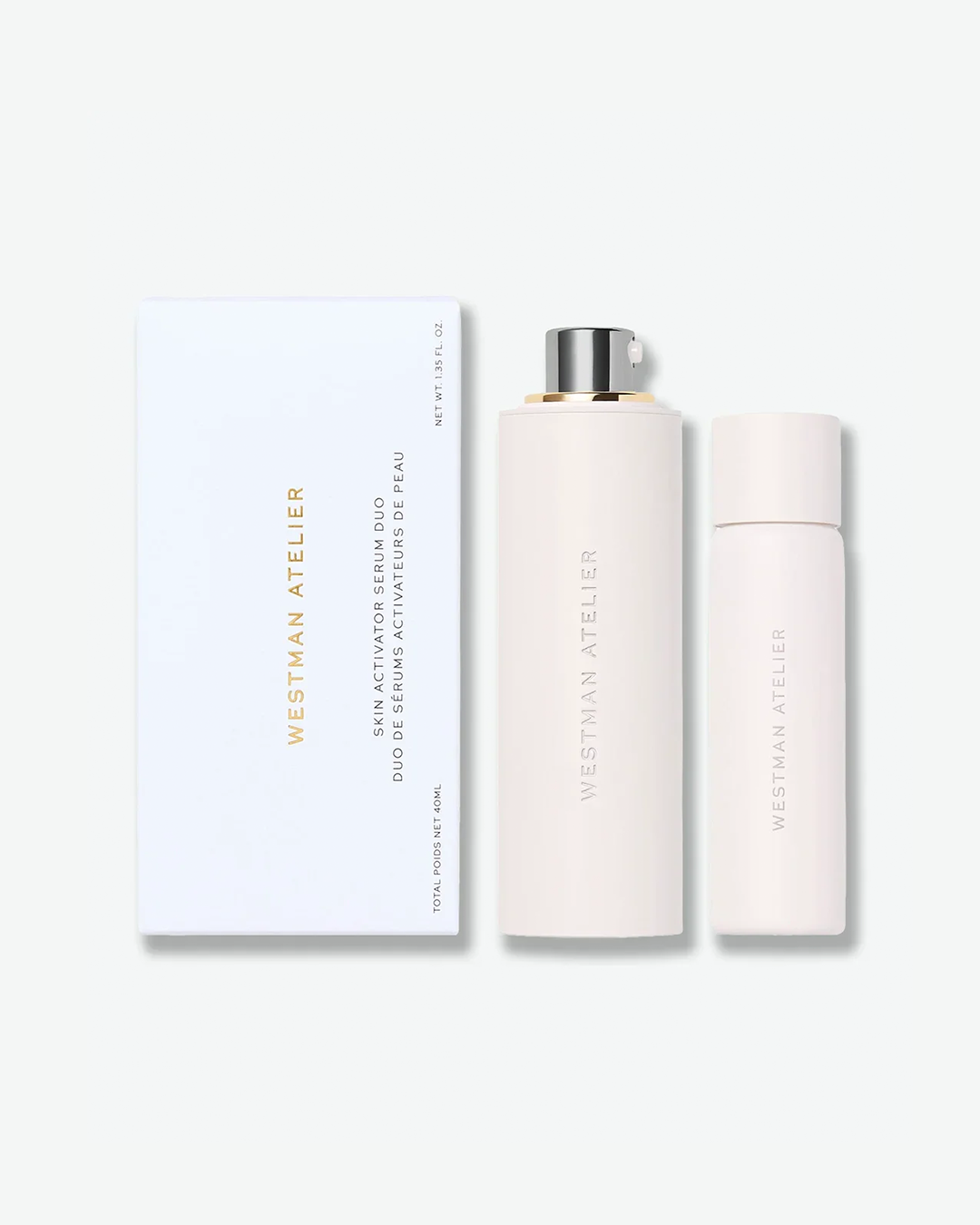 Westman Atelier Skin Activator Serum Duo packaging set featuring a white rectangular box with gold text next to a tall pale pink pump bottle and a smaller matching travel-sized bottle, isolated on a light grey background.
