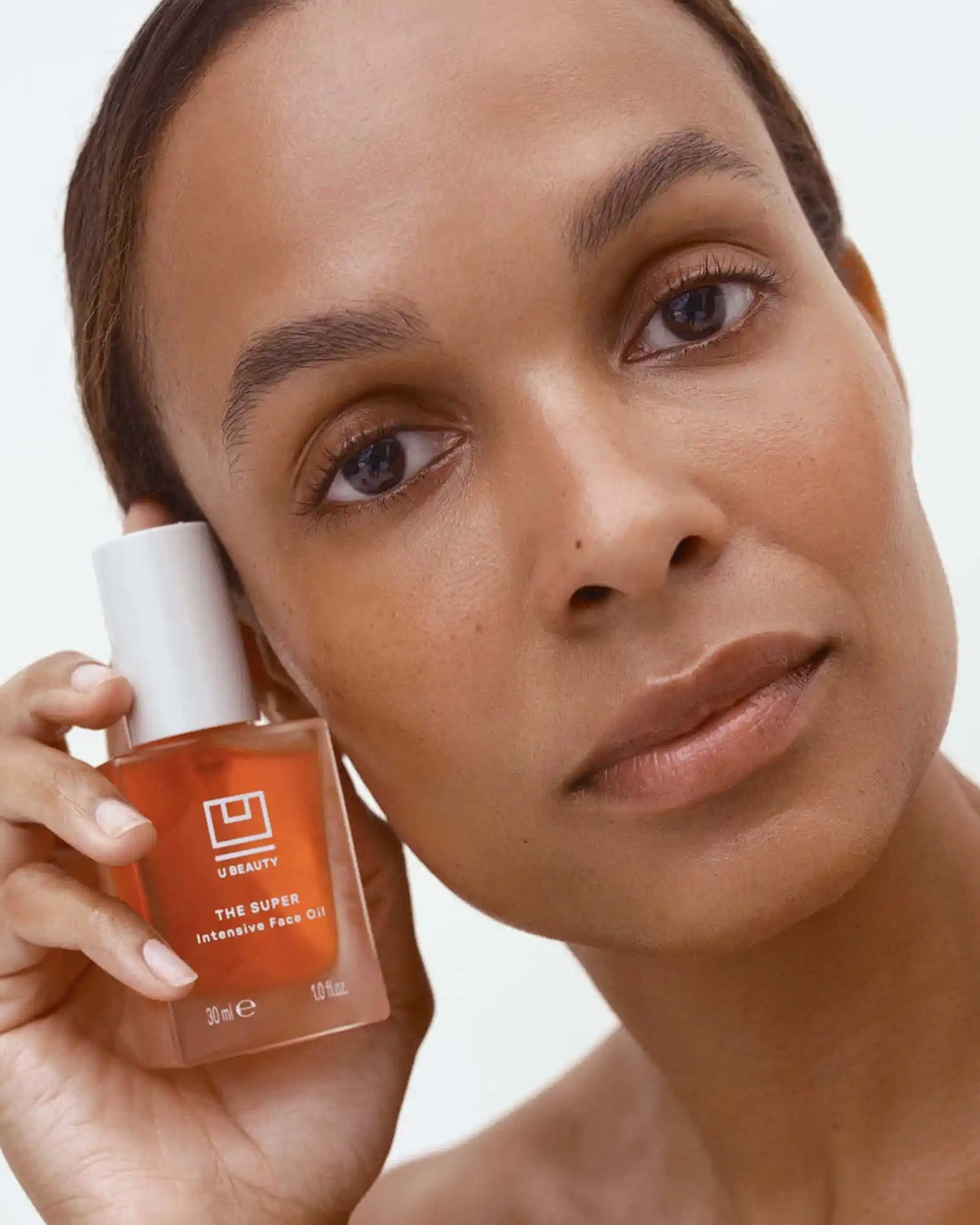 Woman holding a bottle of Ubeauty skincare product against a neutral background