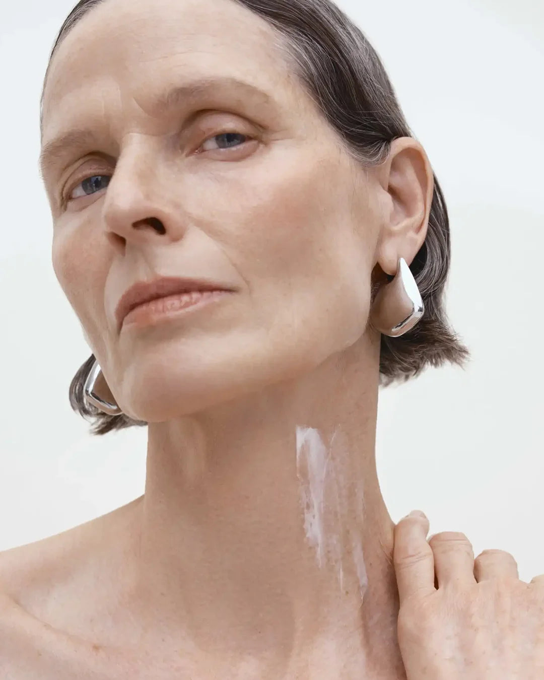 Woman applying sunscreen to her neck with a white background