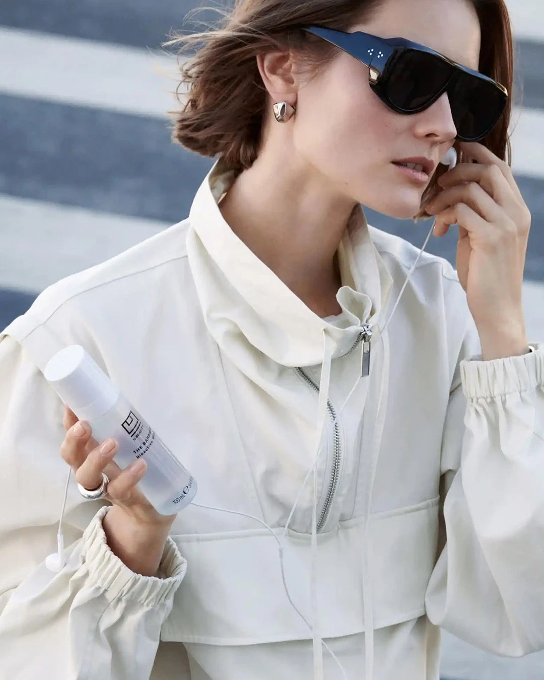 Woman in white jacket and sunglasses holding a white spray bottle with text.