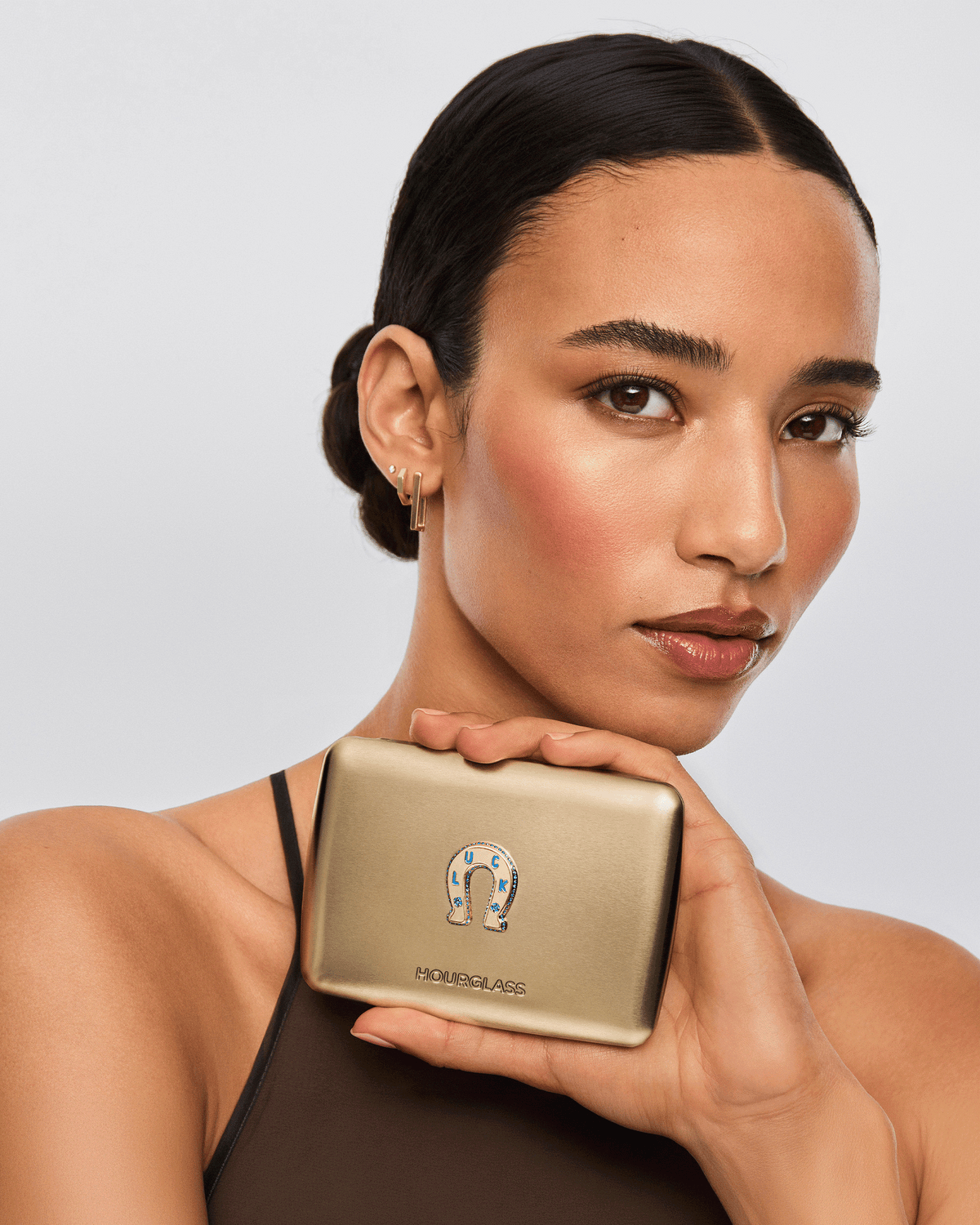 Model holding the closed gold Hourglass Ambient Lighting Edit – Unlocked Palette in Luck, featuring the decorative Luck horseshoe emblem.