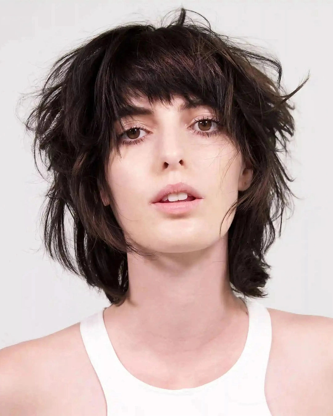 Person with messy dark brown hair wearing a white tank top against a plain background