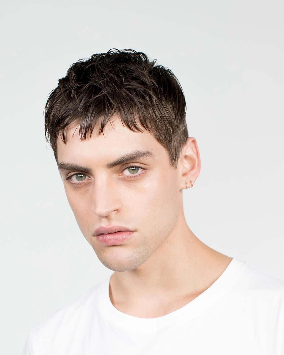 Man with short dark hair wearing a white shirt against a light gray background